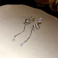 Detailed close-up of asymmetrical bow earrings with sparkling crystal tassels on a dish - Silver Needle / Silver