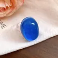 Macro detail showing the glossy finish of a vintage blue oval resin ring on white cloth. - Blue