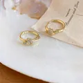 Macro detail of 14k gold-plated knot hoop earrings with sparkling zirconia stones - Gold