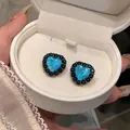 Nahaufnahme von herzförmigen Ohrsteckern mit blauem Opal und schwarzem Zirkonia in Geschenkbox - Blau
