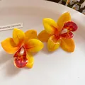 Dettaglio di orecchini a lobo a forma di orchidea gialla e arancione in resina su piatto - Stile Orchidea (HE31628) / Giallo