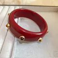 Vue détaillée d'un bracelet jonc rétro en résine rouge avec d'élégants rivets dorés - Rouge