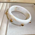 Gros plan sur un bracelet en résine vintage avec marbrure ambre et clous dorés élégants. - Blanc