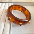 Gros plan d'un bracelet jonc en résine ambre avec des détails de clous en métal doré - Marron