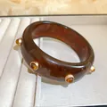 Gros plan d'un bracelet vintage en résine marron avec rivets décoratifs dorés - Café Foncé