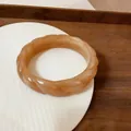 Primo piano di un bracciale in acrilico caramello con elegante trama a spirale. - Cachi
