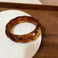 Macro di un bracciale in acrilico ambra con bordi ondulati e motivo a guscio di tartaruga - Marrone