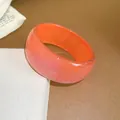 Detailed view of a wide orange resin bangle with a shimmering glitter finish and smooth texture - Orange