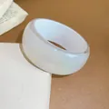 Close-up of white iridescent resin bangle with shimmer on a textured display box. - White