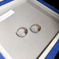 Close-up van elegante zilveren oorringen bezet met fonkelende zirkonia's in een doosje - Ronde Huggie Oorbel (HE34261) / Zilver