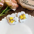 Detailansicht der übergroßen weiß-gelben floralen Ohrringe auf einem dekorativen weißen Teller - Blumenstil (HE33224) / Weiß Und Gelb