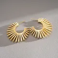 Detailed close-up of gold sunburst C-shaped hoop earrings on grey textured leather background. - Silver Needle / Gold