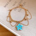 Detailed close-up of a gold anklet with a blue oil-dripping flower pendant and beads. - Blue Flower / Gold