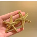 Primo piano di orecchini a stella marina dorati con texture per uno stile da vacanza. - Stile Stella Marina (HE32782) / Oro