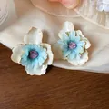 Dettaglio di orecchini a fiore in tessuto con petali di smalto bianco e centro blu - Beige-Blu