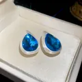 Detailed close-up of blue teardrop stud earrings with brushed silver finish in box - Blue