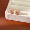 Detalle de cerca de pendientes de botón de flor con circonitas rosas y acabado dorado. - Pendientes / Rosa
