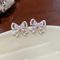 Detailed macro view of delicate hollow silver bow stud earrings with a pearl center. - Silver Earring Post - Silver - Pink