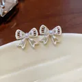 Macro view of delicate hollowed bow-knot earrings with small central pearl detail - Silver & White (Silver Earring Post)