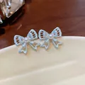 Macro view of delicate silver hollow-out bow stud earrings featuring a central white pearl - Silver Earring Post - Silver - Blue