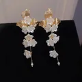 Detail of elegant floral drop earrings with white petals and gold leaf accents on black. - Gold-White