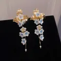Macro detail of French flower tassel earrings with gold leaves, white petals and pearls - Gold-White-Blue