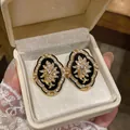 Detailed view of vintage palace style floral gold earrings with rhinestones in a gift box - Black / Gold