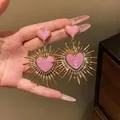 Primo piano di eleganti orecchini a cuore in smalto rosa con raggi solari dorati retrò - Rosa