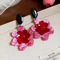 Primer plano de pendientes de flores de acrílico rosa y rojo sobre fondo beige - Rosa y Rojo
