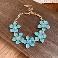 Bracciale vintage dorato con cinque fiori in smalto azzurro su ripiano in legno - Blu