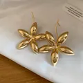 Detaillierte Nahaufnahme von glänzenden goldenen Blumenohrringen mit Metalloberfläche - Blumenstil (HE32273) / Gold