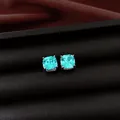 Close-up of square cushion-cut aqua blue zircon stud earrings on black leather. - Square Studs / Light Blue