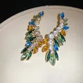 Close-up of elegant wing-shaped earrings with vibrant colorful marquise rhinestones on plate - Gold-Multicolor