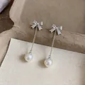 Detailed macro shot of silver bow earrings with zircon stones and elegant white pearl drops. - Bow Tassel / White