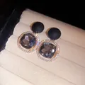 Detailed macro view of elegant matte black and square crystal stud earrings on display. - Black