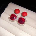 Close-up of red faceted gemstone earrings with sparkling diamond halo on velvet display - Red