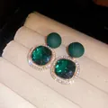 Macro view of elegant emerald green square earrings featuring a crystal halo and matte beads - Green