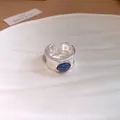 Gros plan détaillé d'une bague ouverte argentée avec pierre ronde bleu foncé sur coquillage - Pierre bleue ronde