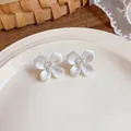Detailed shot of elegant white enamel flower stud earrings with central pearls on a plate - White