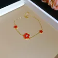 Close-up detail of an elegant gold-plated bracelet with red zircon flower charms. - Bracelet / Gold-Red