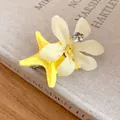 Macro view of a yellow starfish and fabric flower hair clip on a vintage book. - Duckbill Hair Clips / Yellow