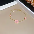 Close-up of gold plated bracelet with sweet pink enamel flowers and sparkling zircon center - Bracelet / Gold-Pink