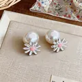 Detailed close-up of sweet enamel daisy and pearl stud earrings on a beige tray - Pink