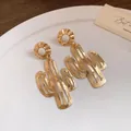 Detailansicht von goldenen Metallohrringen in Kaktusform auf einem weißen Porzellanteller - Gold