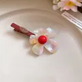 Dettaglio fermaglio per capelli a fiore in acetato iridescente con perla rossa. - Rosso