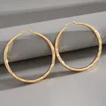 Close-up detail of large gold hoop earrings with elegant textured diamond-cut surface pattern - Gold