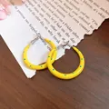 Detail of yellow C-shaped hoop earrings with blue polka dots on a wooden background - 3cm / Yellow