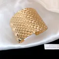 Close-up detail of a wide gold woven texture cuff bracelet resting on white silk fabric. - Square Weave Texture / Gold