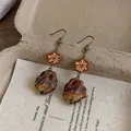 Close-up of vintage ethnic drop earrings with carved wood flower and seed pod detail - Earring Hooks / Brown