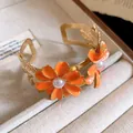 Close-up of golden double-layer cuff bracelet with orange enamel flowers and pearls - Orange